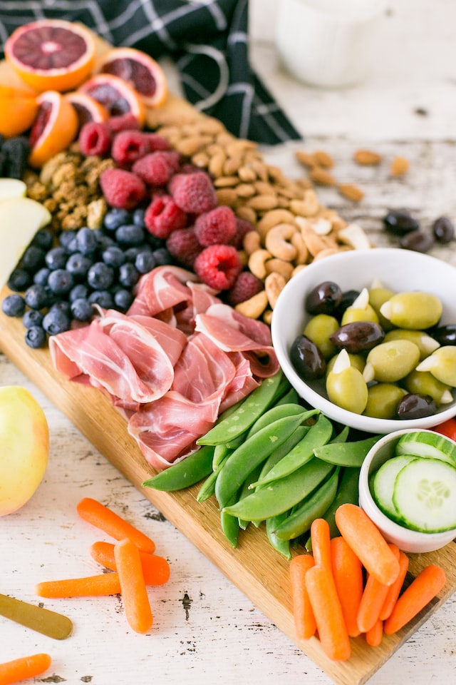 The paleo diet has foods that a cavemen would eat. The picture shows a charcuterie board covered in fruits, veggies, meats, and nuts.