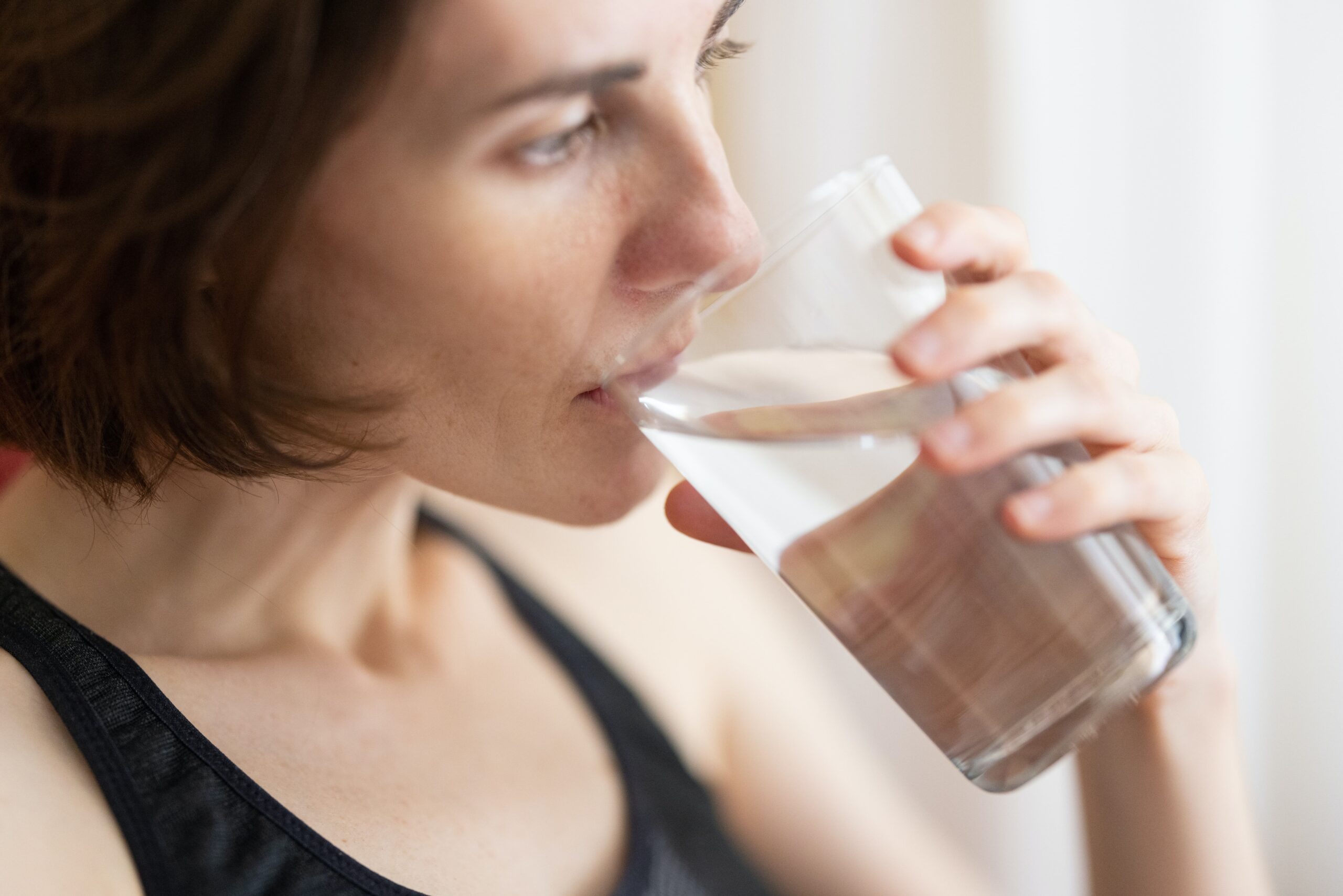 Anti-aging tip about the importance of drinking water. A photo of a woman hydrating by drinking a glass of water.