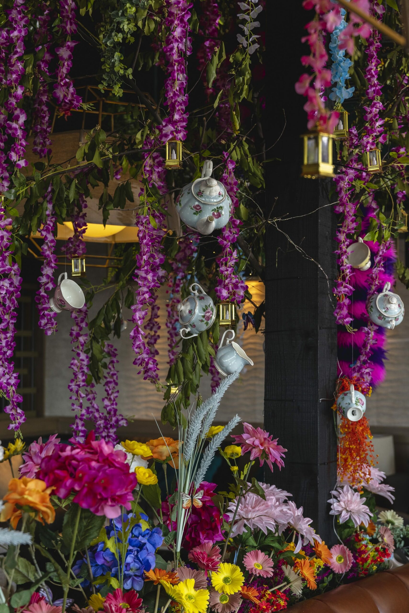 An image of the decor for The Green Room's Through the Looking Glass pop-up. The photo has tea pots, colorful flowers and the famous Cheshire cat.