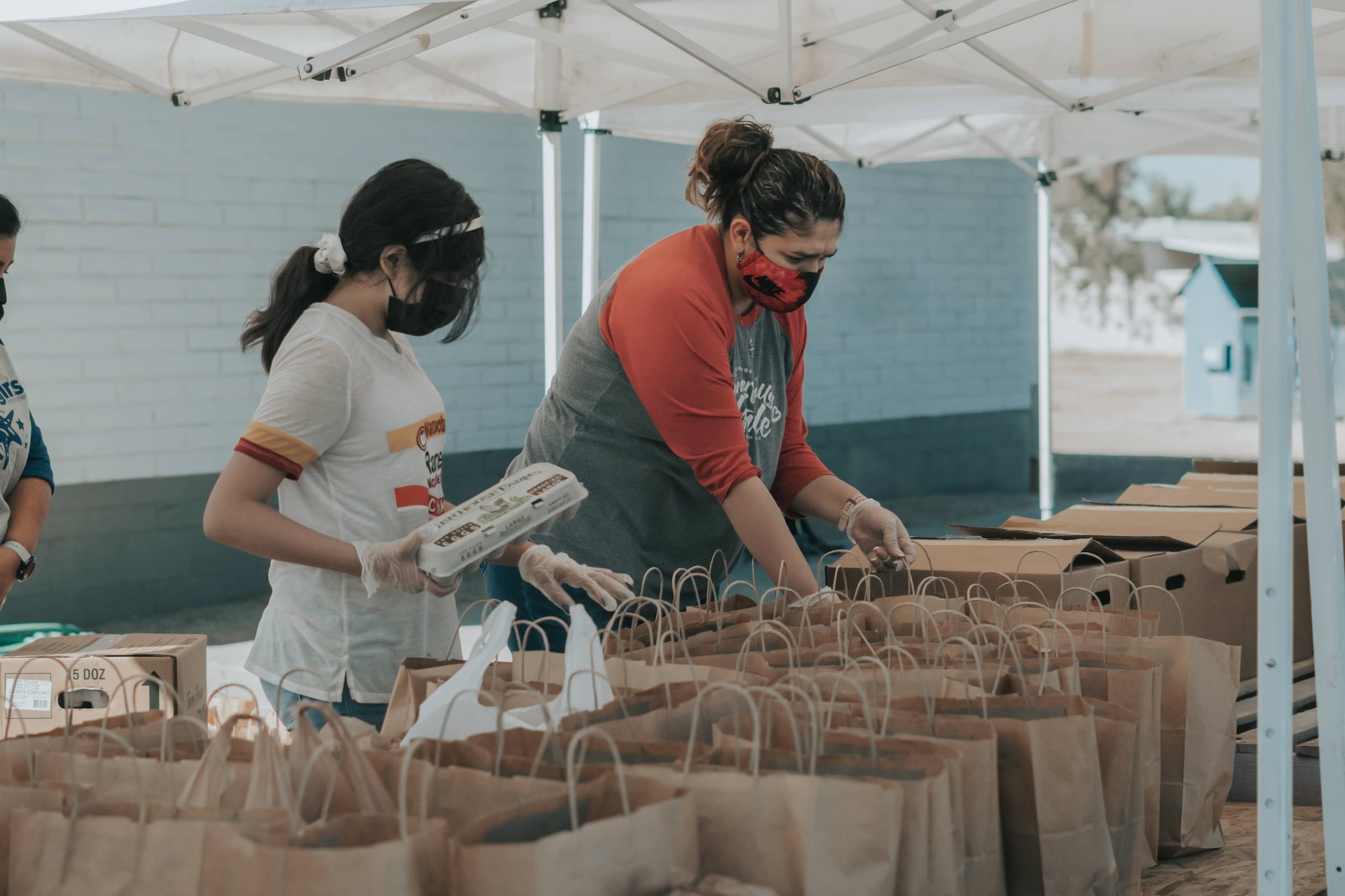 An image of two people volunteering by filling food bags for the homeless.