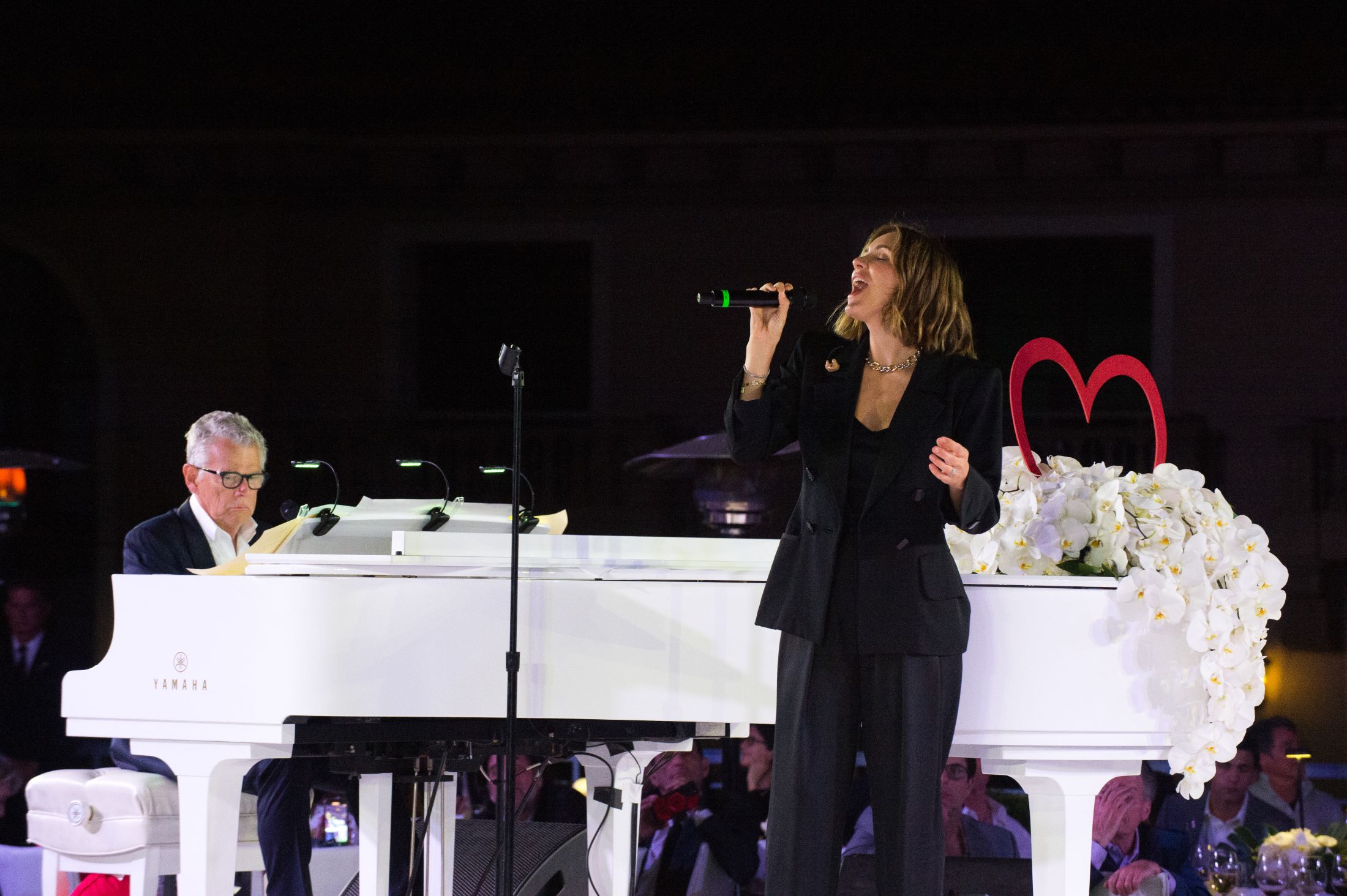 An image of David Foster at the piano and Katharine McPhee singing. 