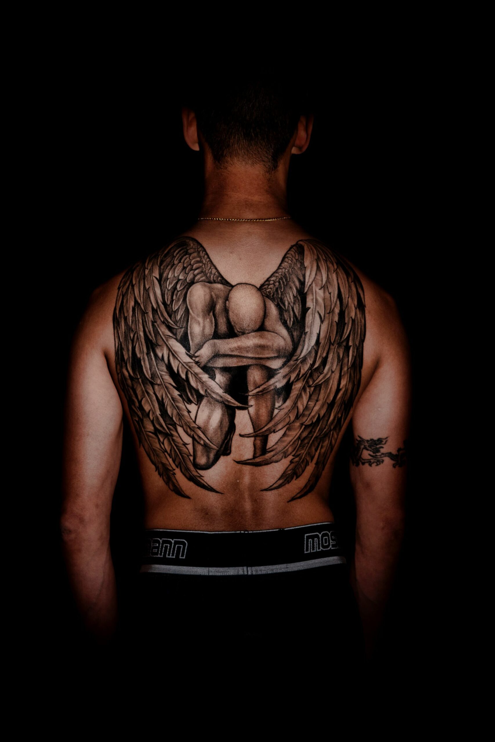 An image of a man's back with an angel and its large wings.