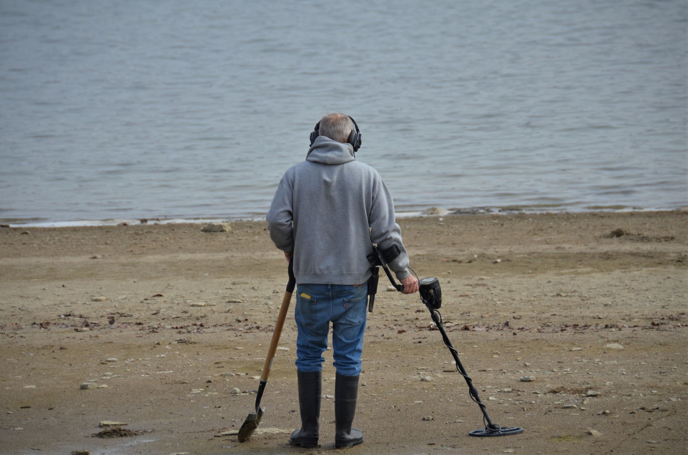 An image of a man on the beach with a shovel and a metal detector.