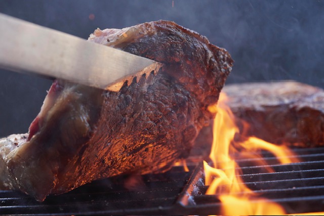 An image of a steak cooking on a grill. 