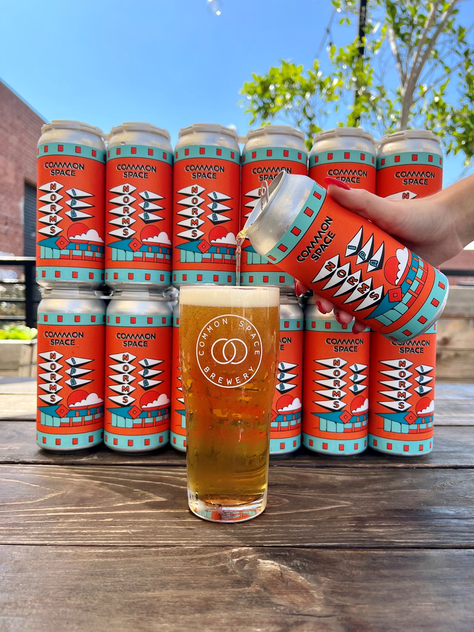 An image of cans of NORMS new IPA, and someone pouring a can into a glass.