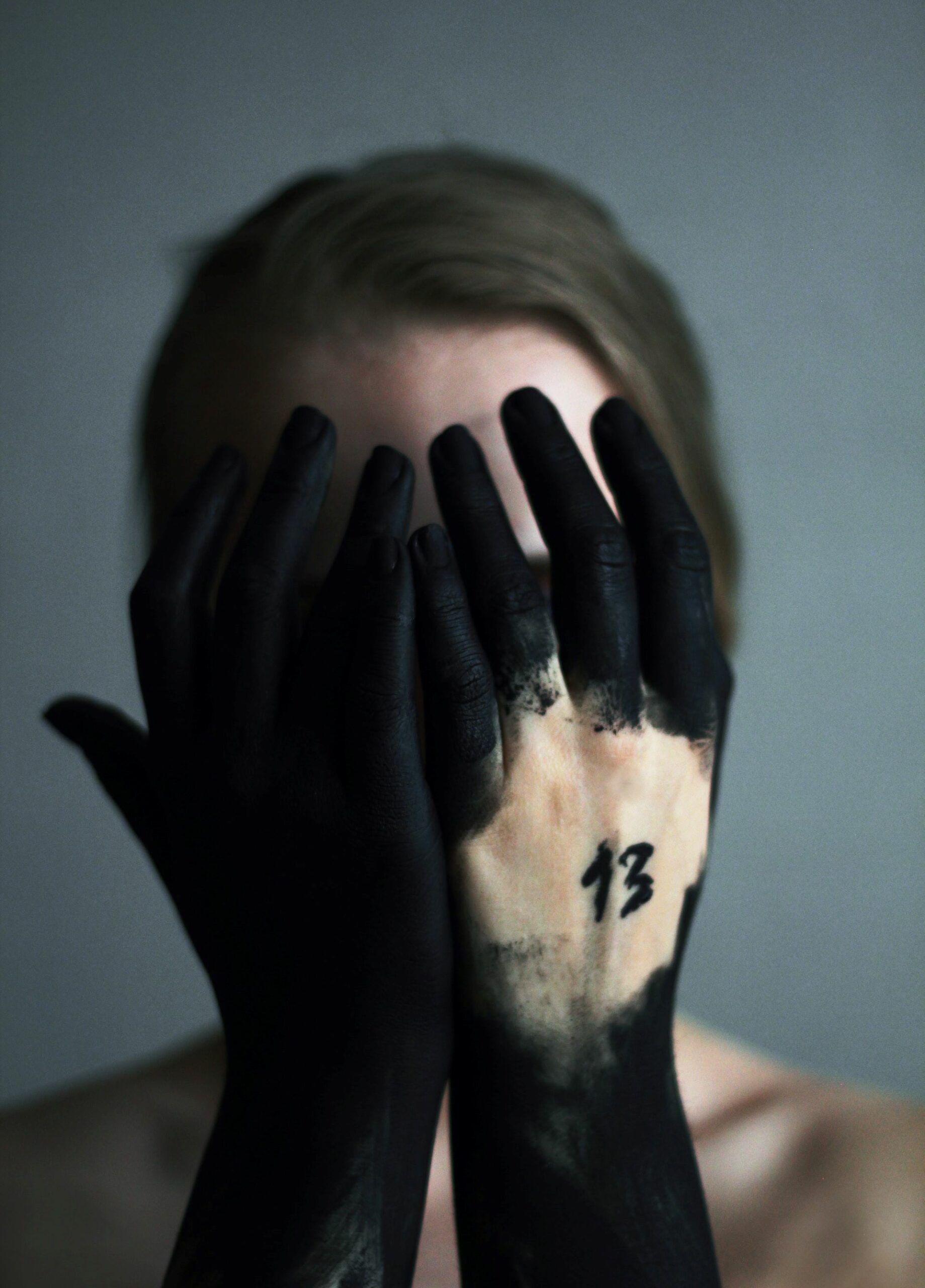 An image of a person with the number 13 on their hands which are hiding their face. 