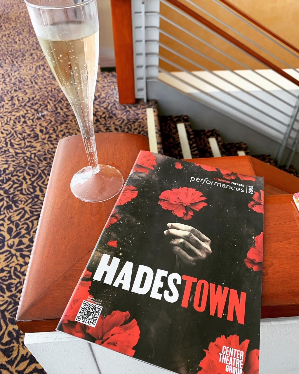 An image of the playbill for HADESTOWN and a glass of champagne. 