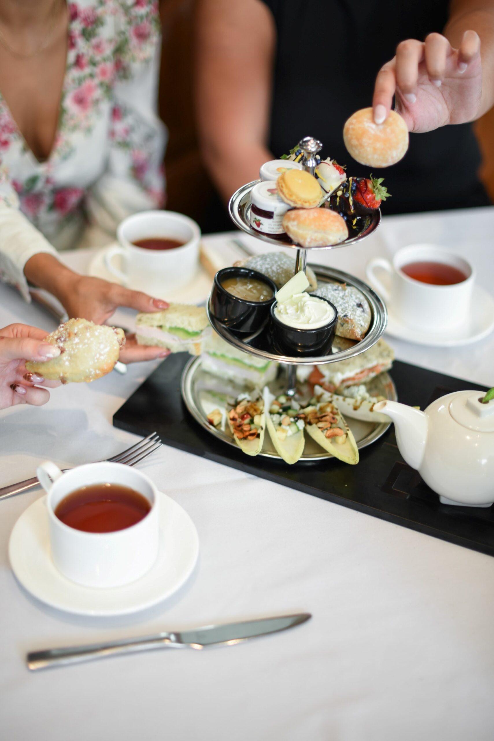 An image of people drinking tea and a tower of tea sandwiches and desserts.