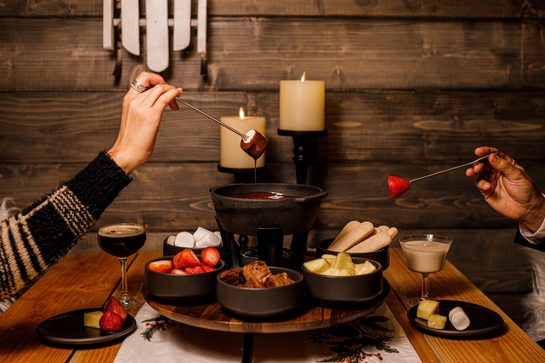 An image of two people eating chocolate fondue with fruit and marshmallows.