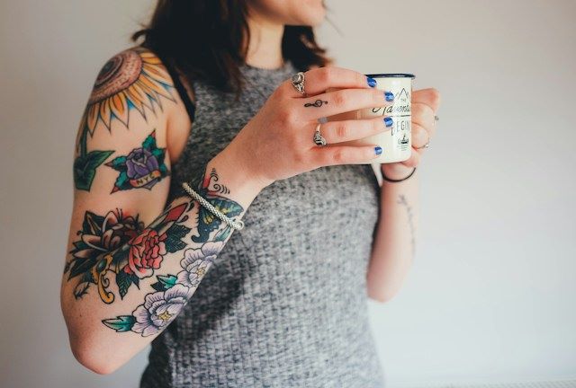 An image of someone holding a coffee cup with a full sleeve tattoo.