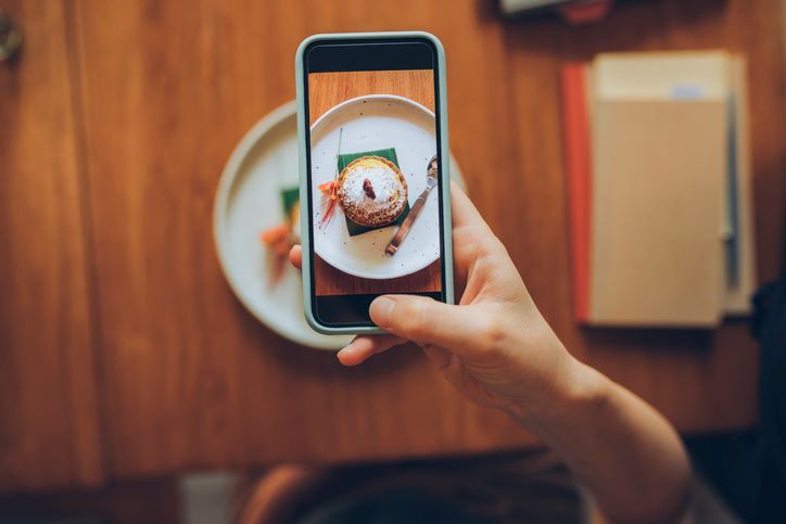 An image of someone taking a photo on their phone of food.