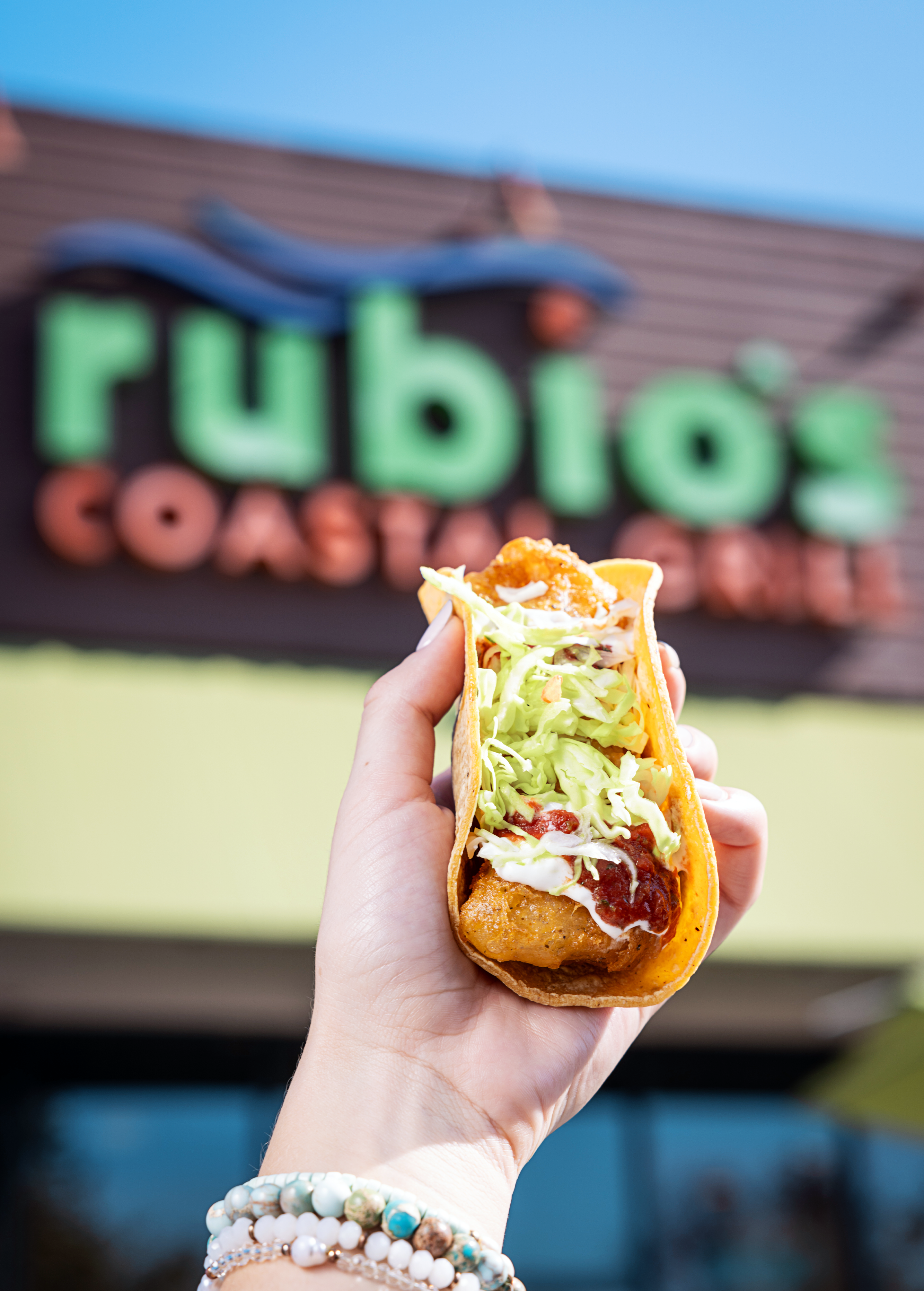 An image of a person holding a fish taco outside of Rubio's. 