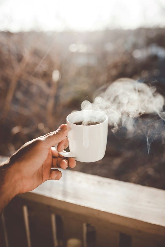 An image of someone holding a cup of coffee with steam coming out of it.
