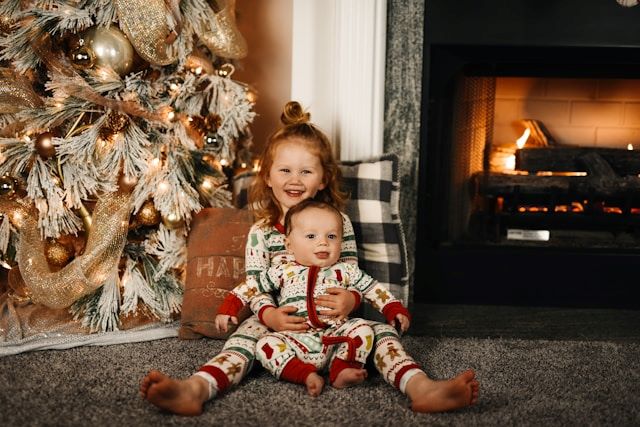 An image of two kids in Christmas pyjamas by a cozy fire.