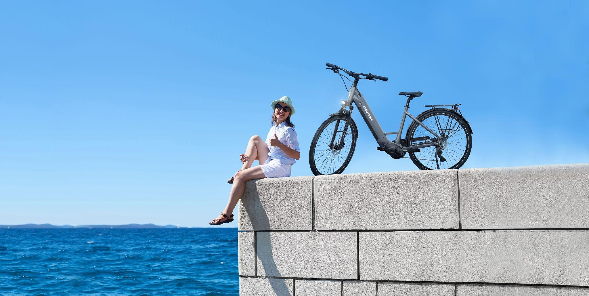 An image of a woman and her e-bike at the beach.