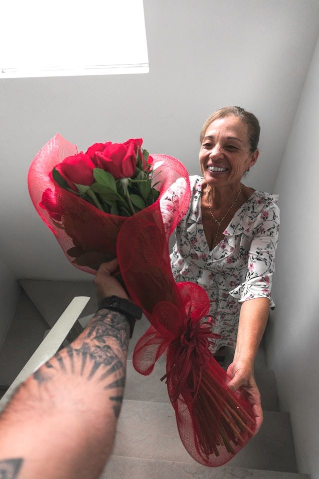 An image of a person giving a woman a bouquet of red roses.