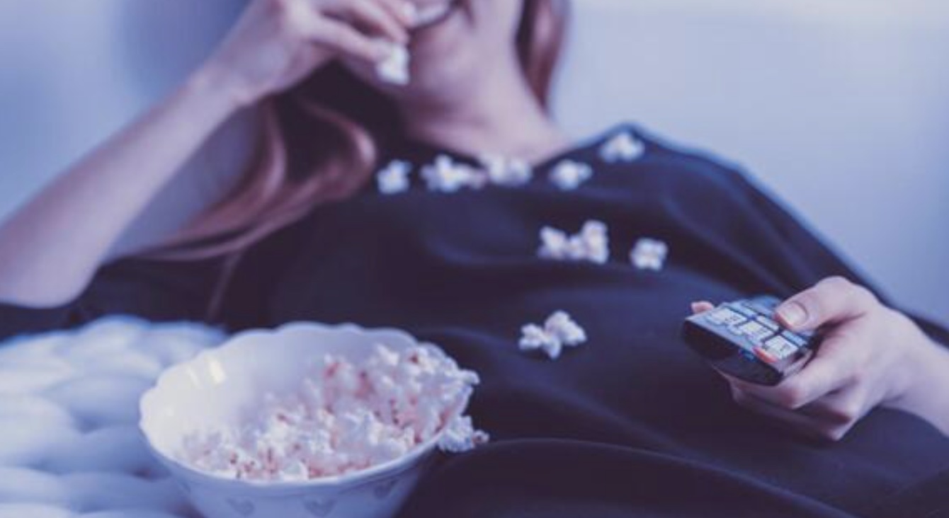An image of a woman eating popcorn on the couch watching the best true crime documentaries.