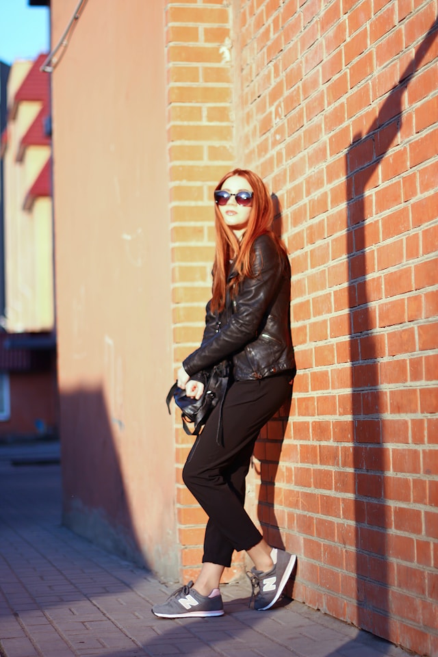 An image of a woman posing up against a wall wearing New Balance sneakers.