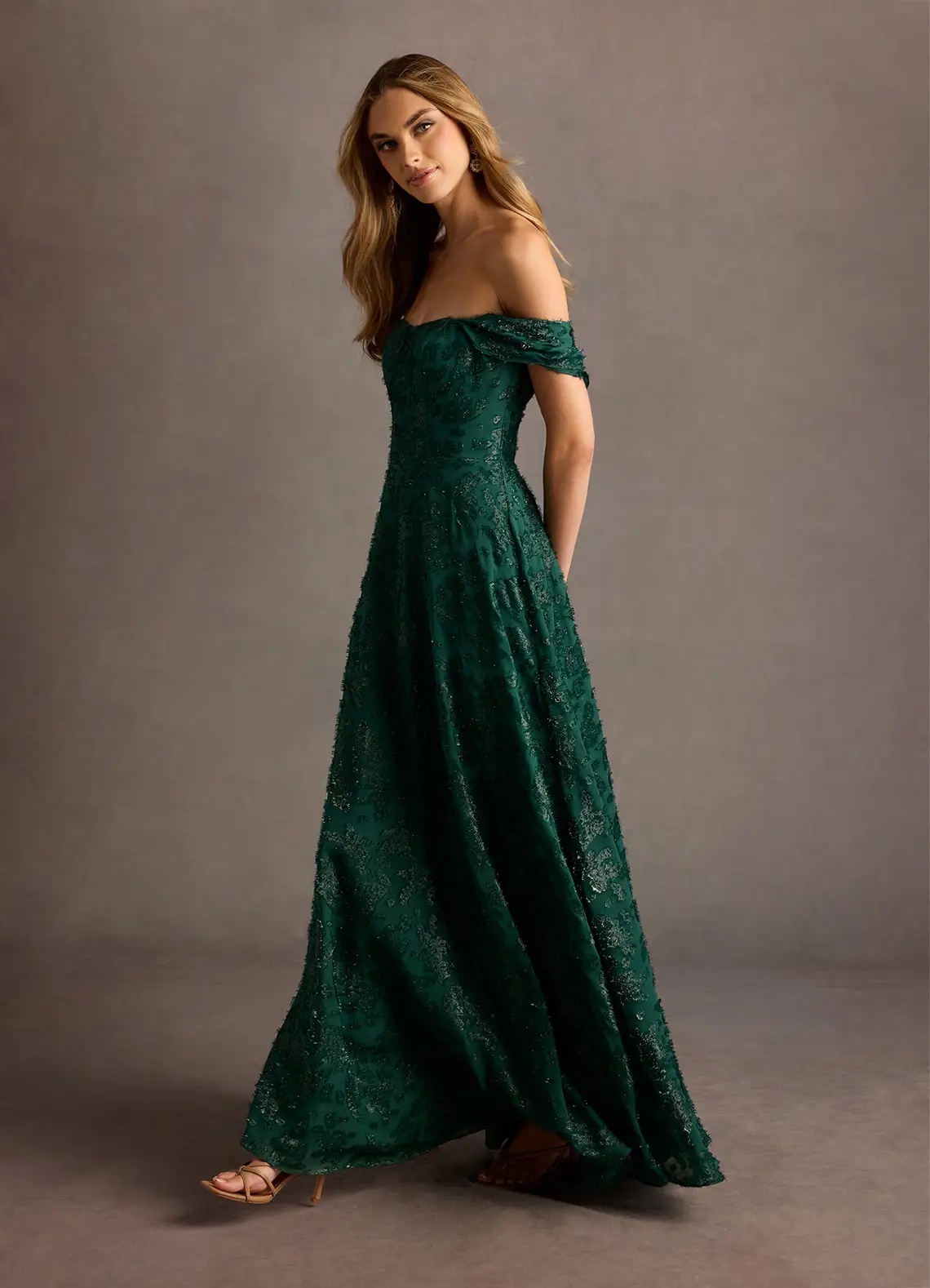 An image of an example of what to wear to a fall wedding, a woman in an emerald green wedding guest dress from Azazie.