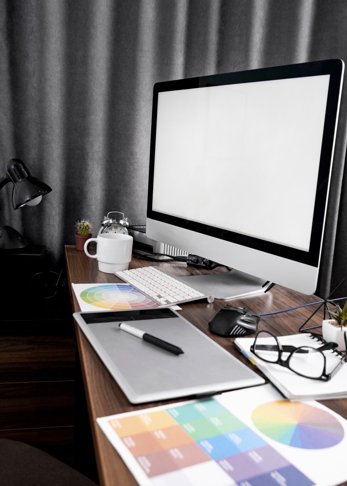 An image of a computer and design paperwork on the desk.