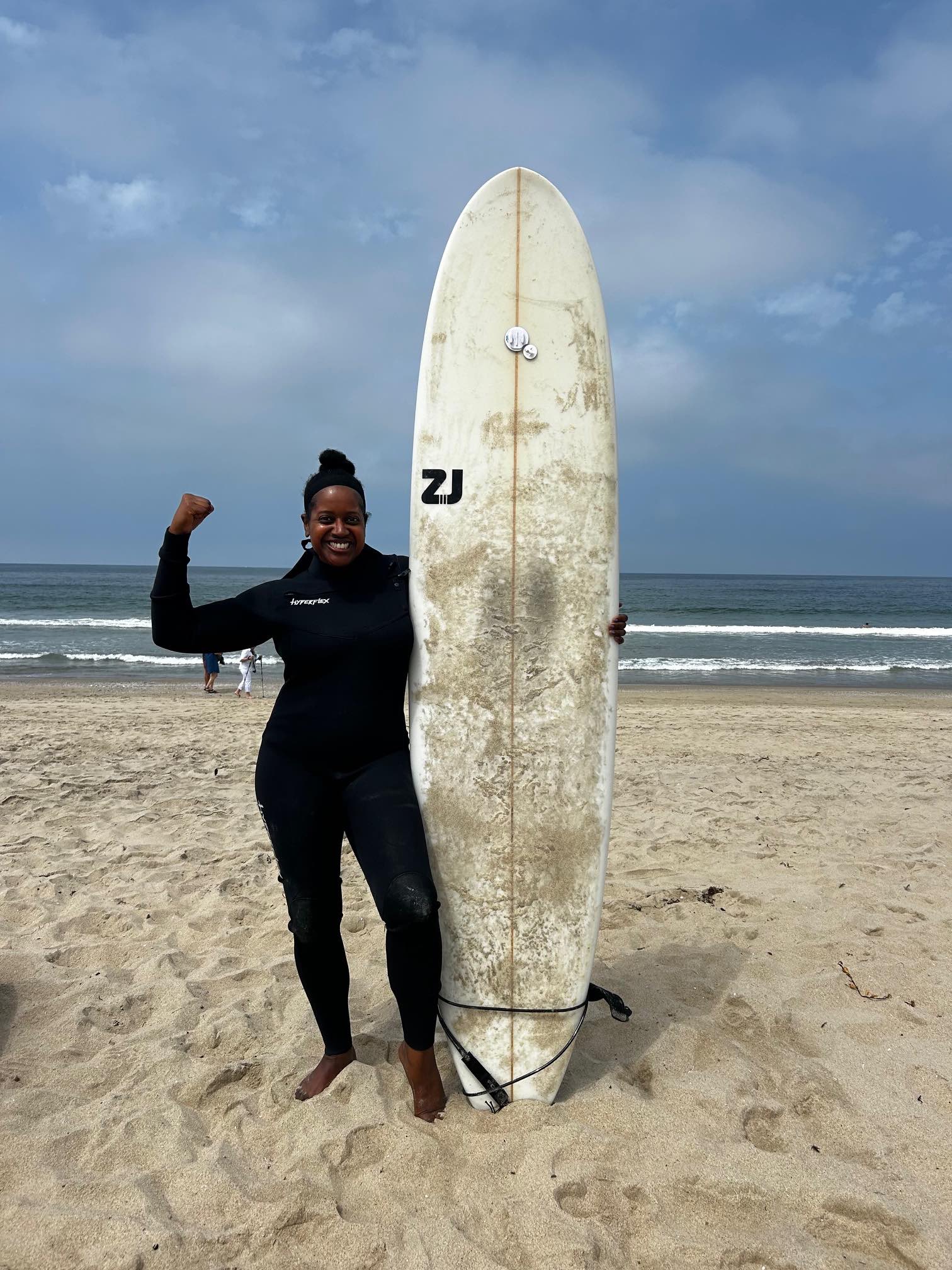 An image of lifestyle blogger Ariel with a surfboard at Happy Yoga beach sessions.