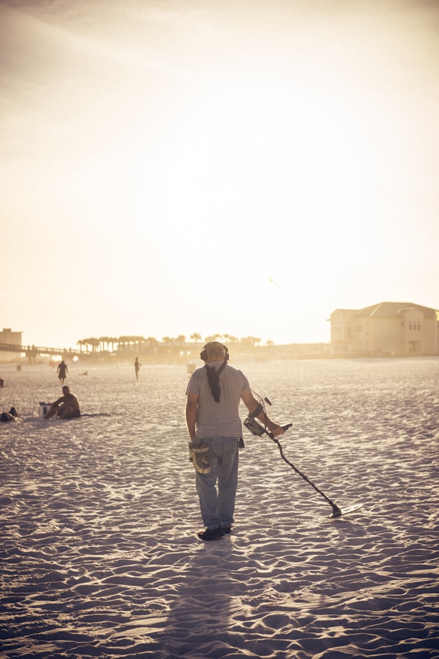 An image of a man treasure hunting on a beach with a metal detector.