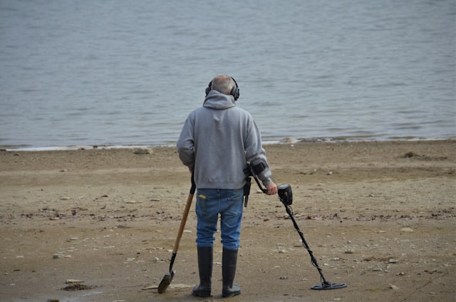 An image of a man walking on the beach with a metal detector.