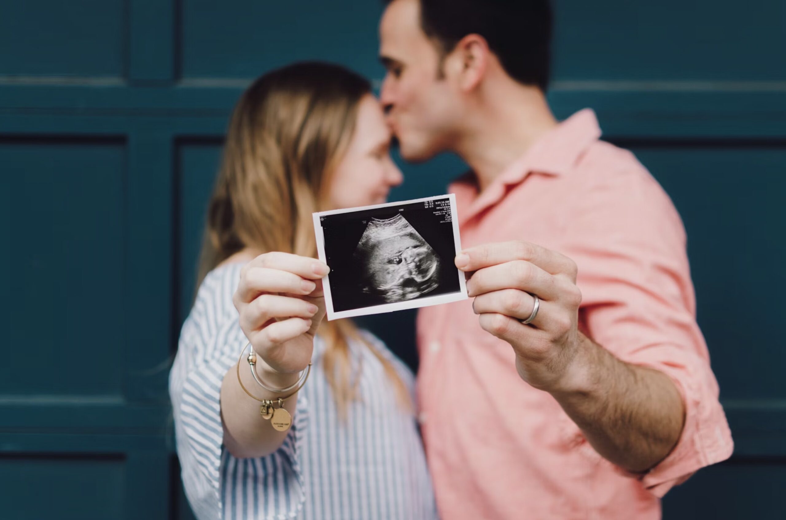 An image of a couple kissing holding a sonogram.