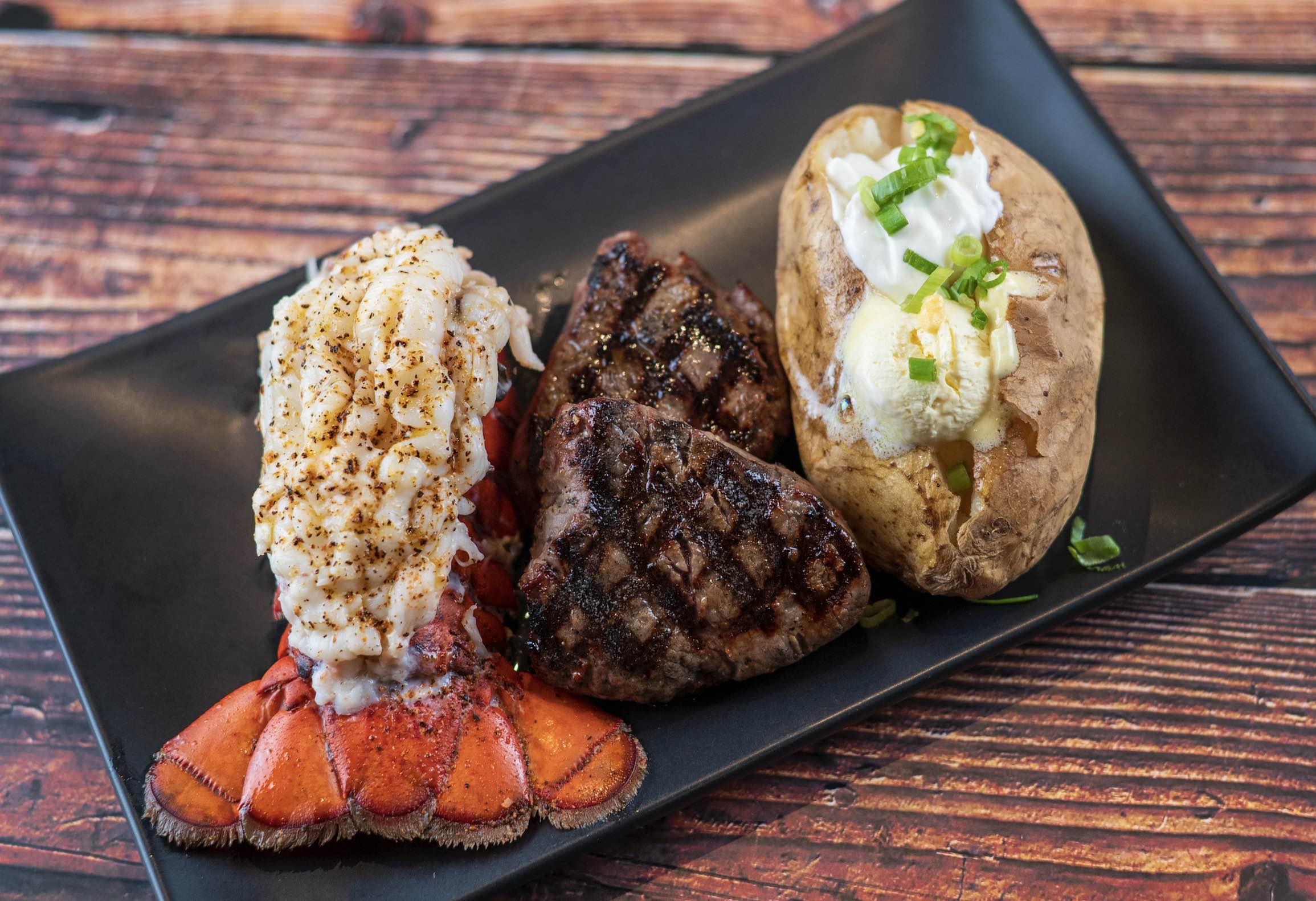 An image of Black Angus' Whole Lobster Tail & 2 Filet Mignon Medallions (3oz) with a baked potato.