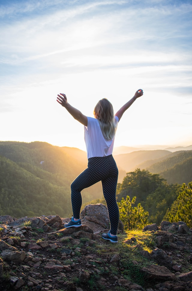 An image of a woman celebrating reaching the top of the mountain she just hiked.