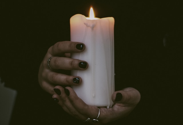 An image of a hand holding a candle for The Witch's Hand cocktail paired with one of the best scary movies for your Halloween party ideas.