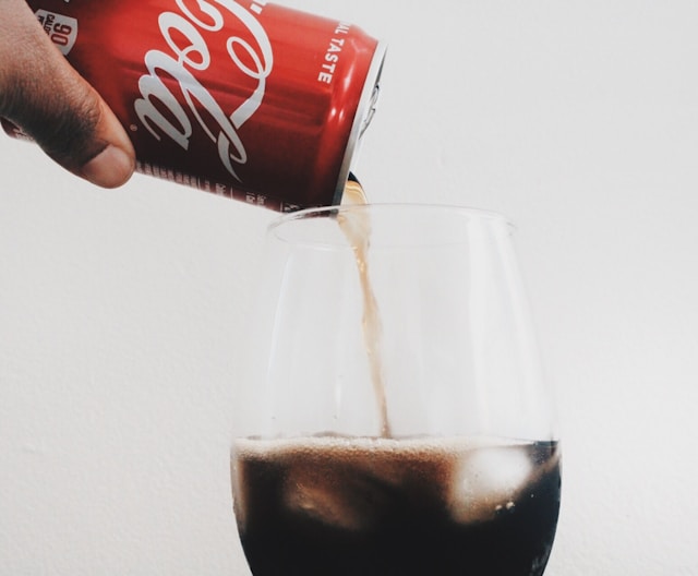 An image of someone pouring a can of coke into a glass to make the MomTok dirty soda recipe for the Dirty Coke.