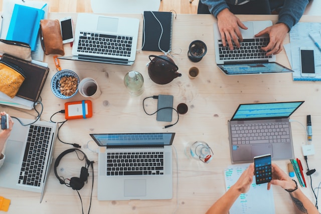 An image of several people at a desk with several laptops.