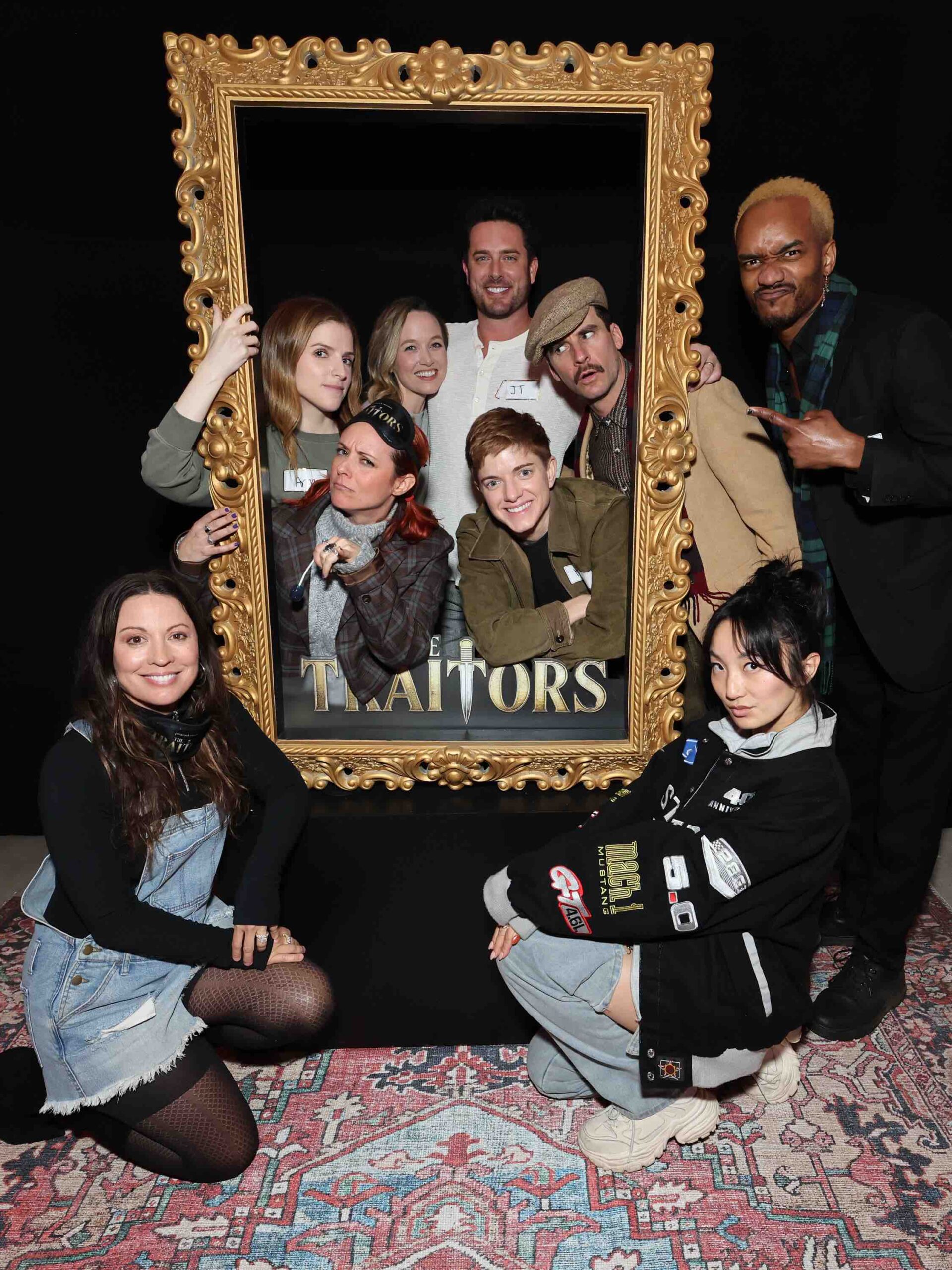 An image of Anna Kendrick (l holding frame), Kelley Jakle (next to Kendrick), Poppy Liu (bottom r) and friends pose for a photo after playing The Traitors VIP Experience.