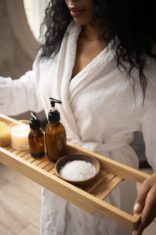 An image of a woman wearing a robe carrying a tray of bath items.