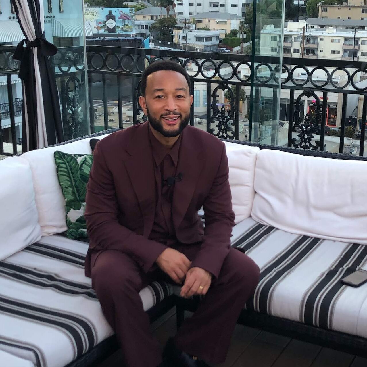 An image of John Legend sitting on a chair with striped seats.