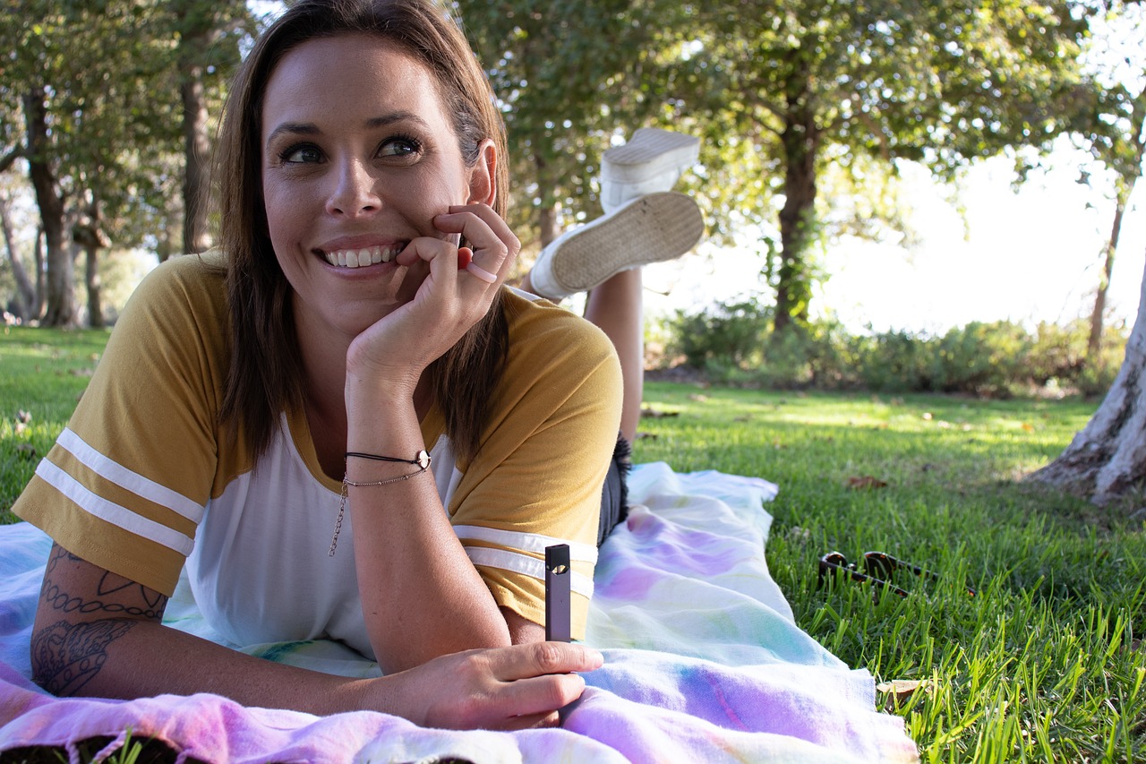 An image of a woman laying in the grass holding a vape pen.