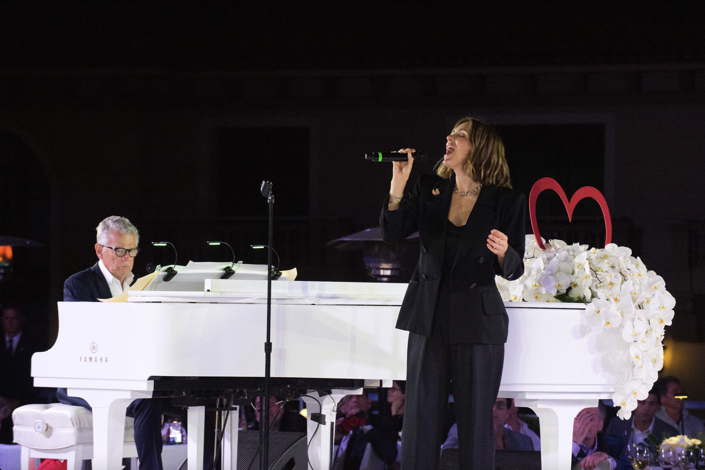 An image of David Foster playing the piano while his wife Katharine McPhee sings.