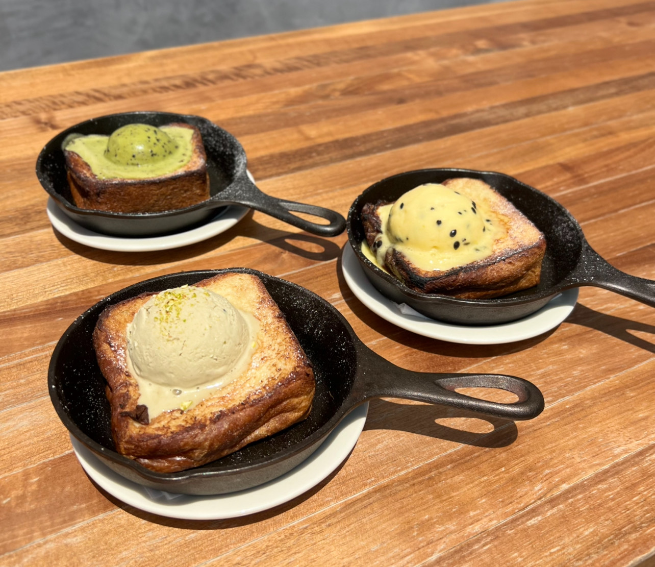 An image of three skillets with French toast topped with different flavors of ice cream.
