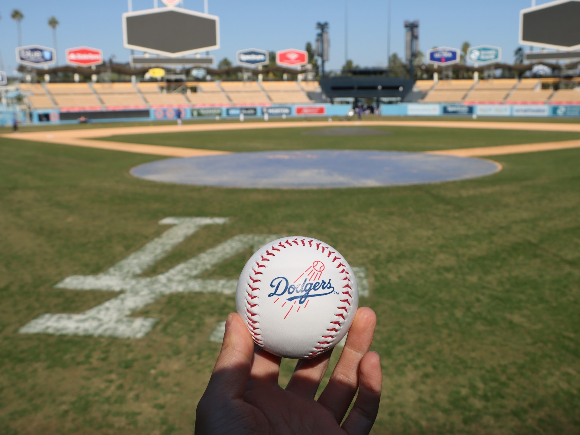 An image of someone holding a Dodgers baseball on Dodgers stadium.