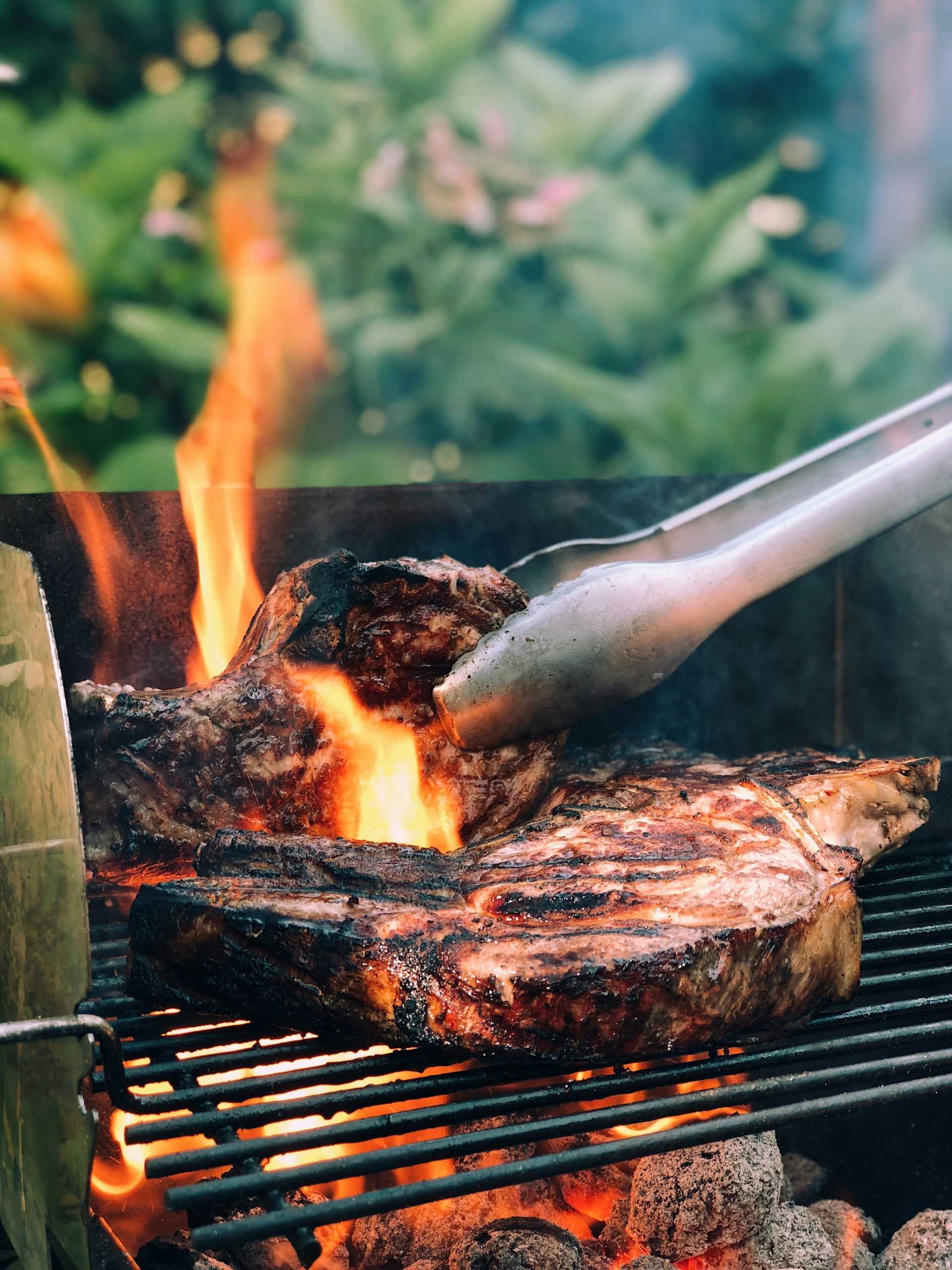 An image of steaks cooking on a grill.