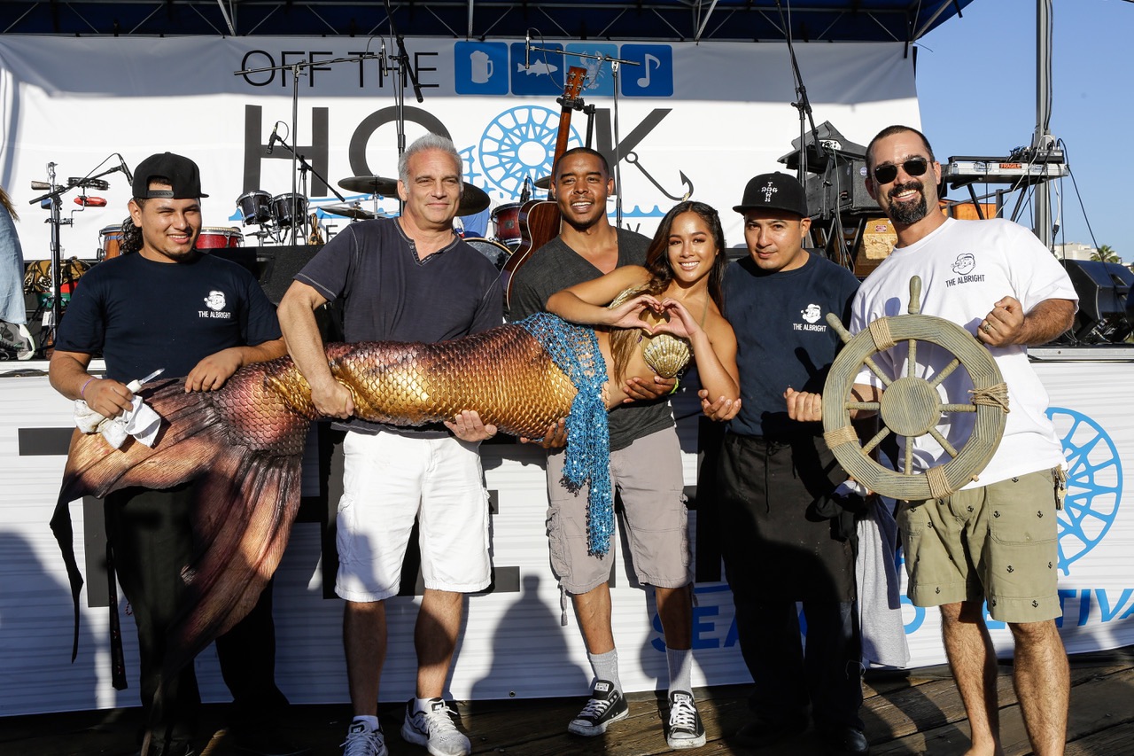 An image of men holding up a woman dressed as a mermaid.