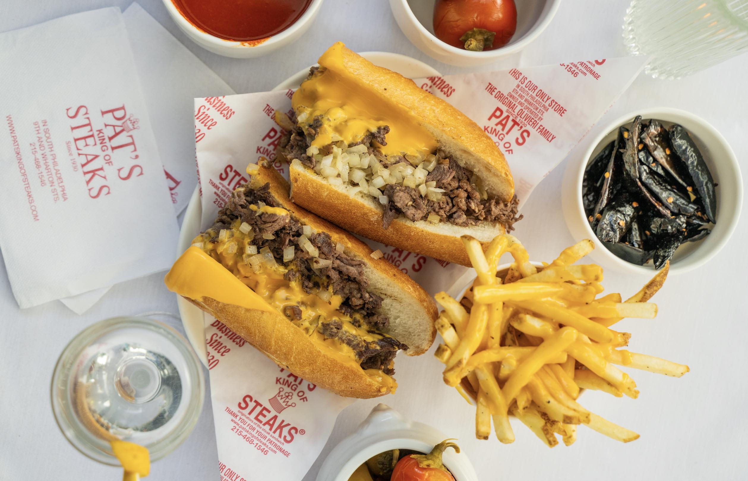 A birdseye image of cheesesteak, cheese fries, a martini from the  Pat’s King of Steaks x The Benjamin collab.