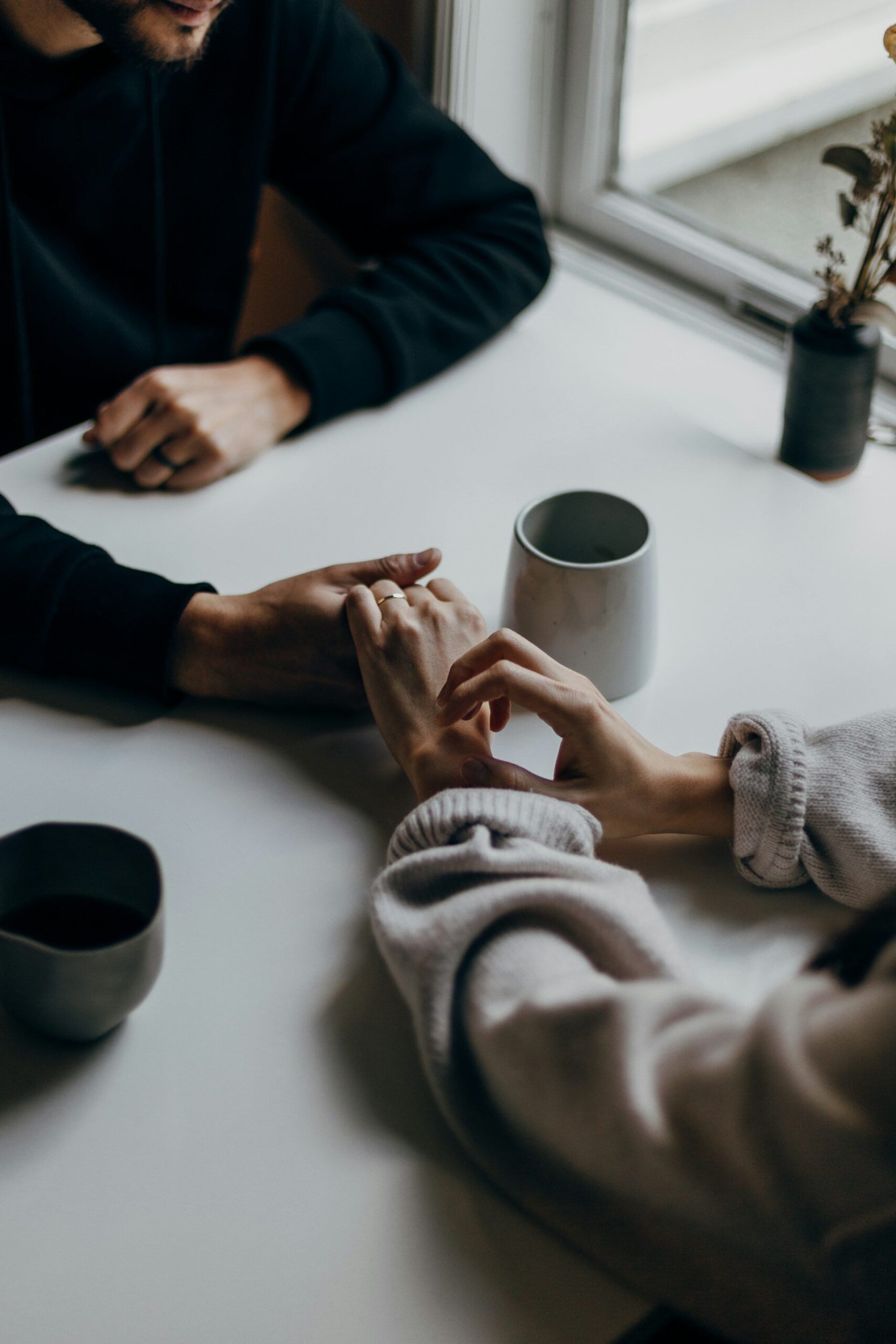 An image of two people holding hands over a cup of coffee.