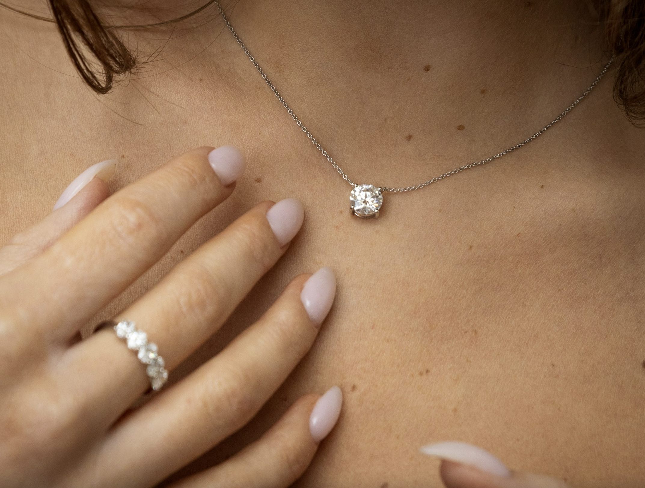 An image of a woman wearing a diamond necklace and diamond ring.