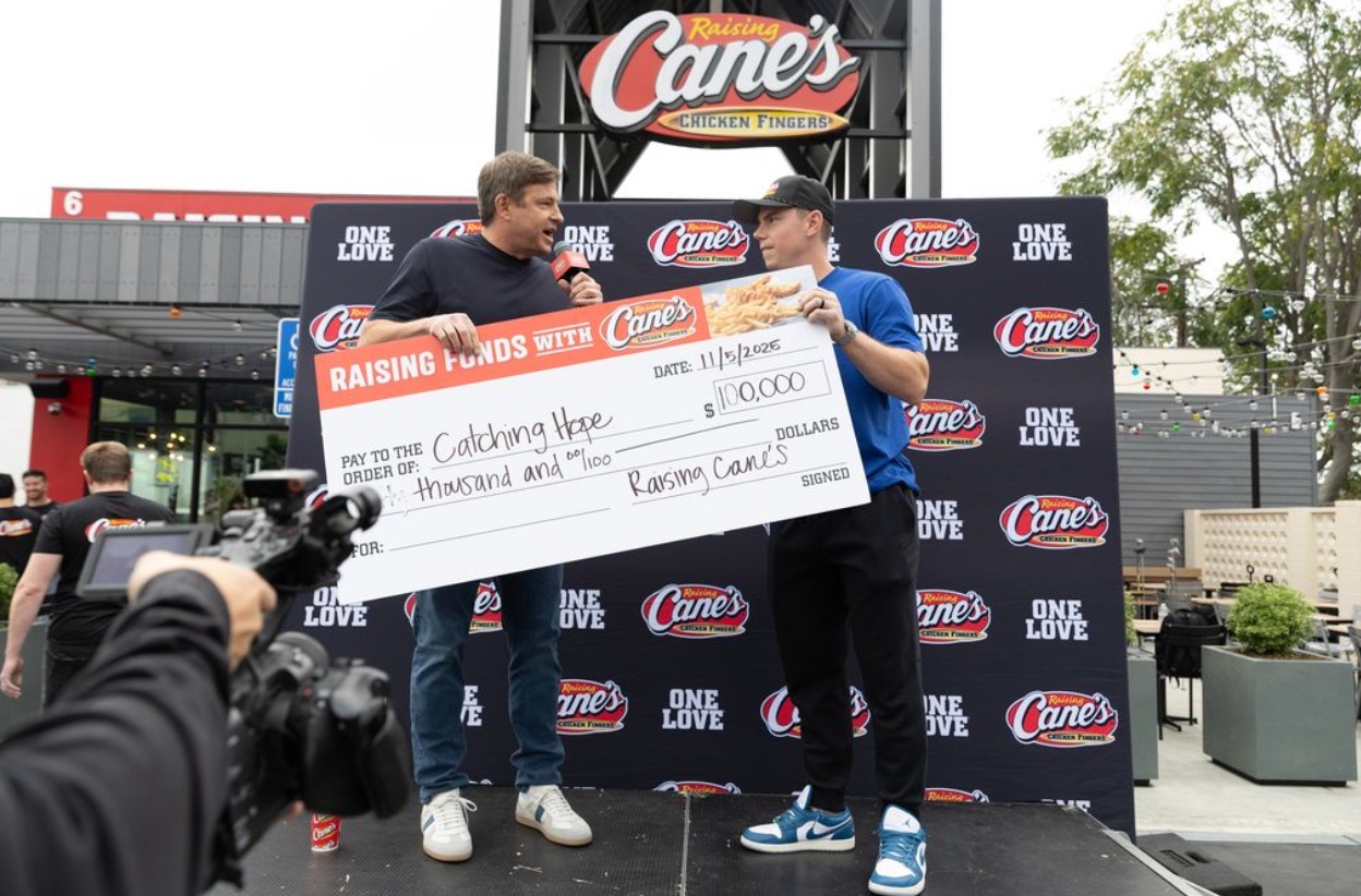 An image of Dodgers Catcher Will Smith Accepting at $100,000 check to his foundation Catching Hope from Raising Cane’s Owner and Founder Todd Graves