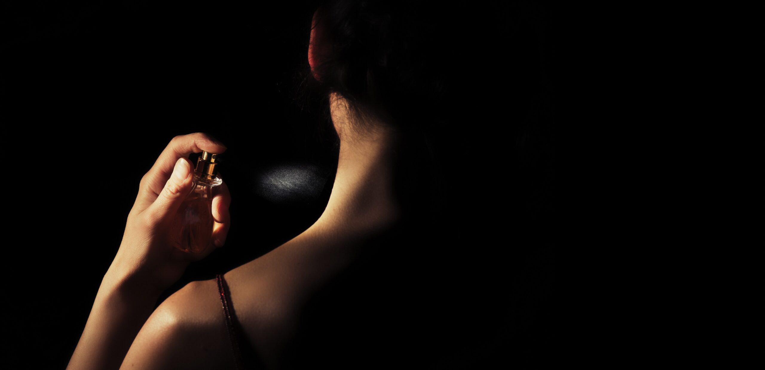 An image of a woman applying perfume to her neck.