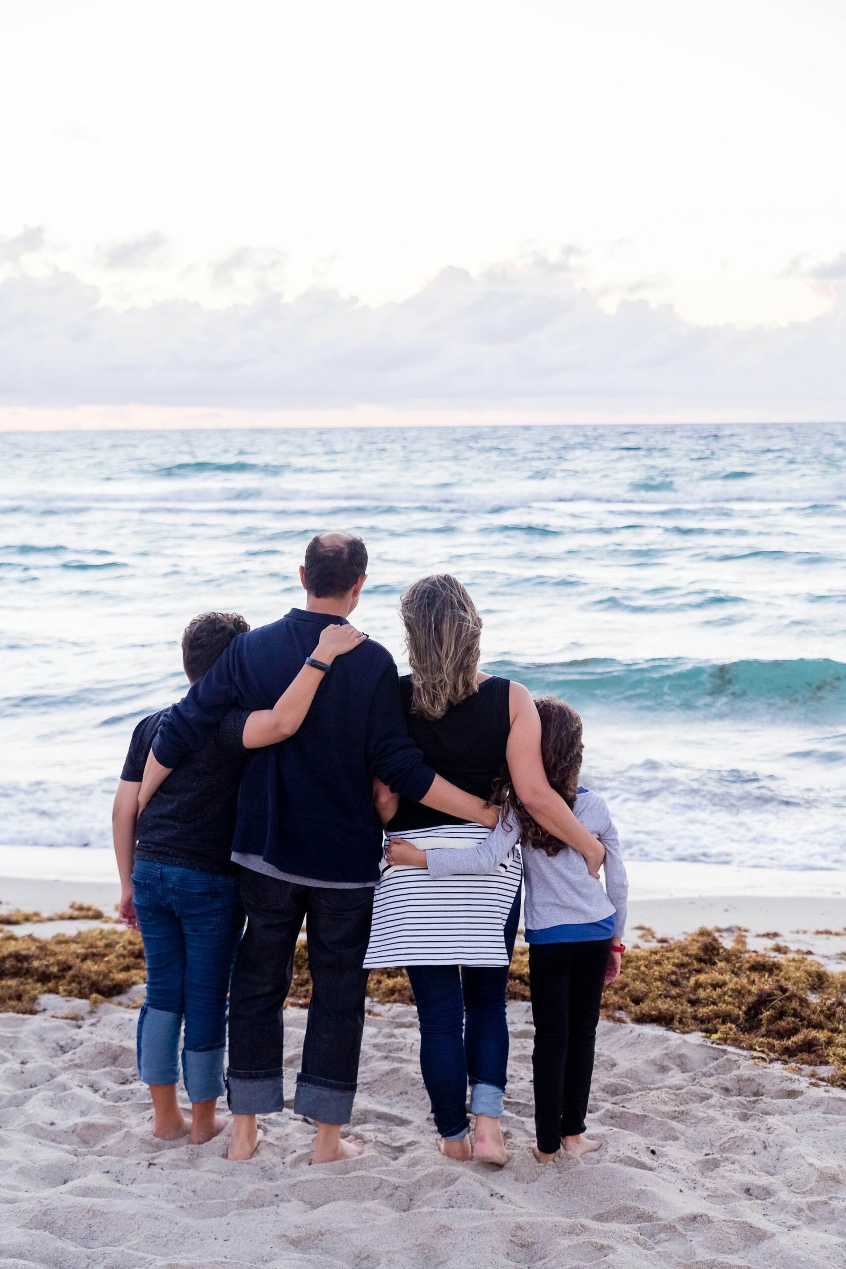 An image of a family posing from the back at the beach.