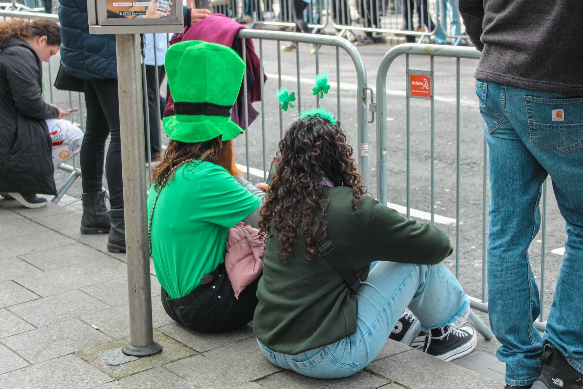 An image of people sitting at on the ground at a St. Patrick's Day Parade.