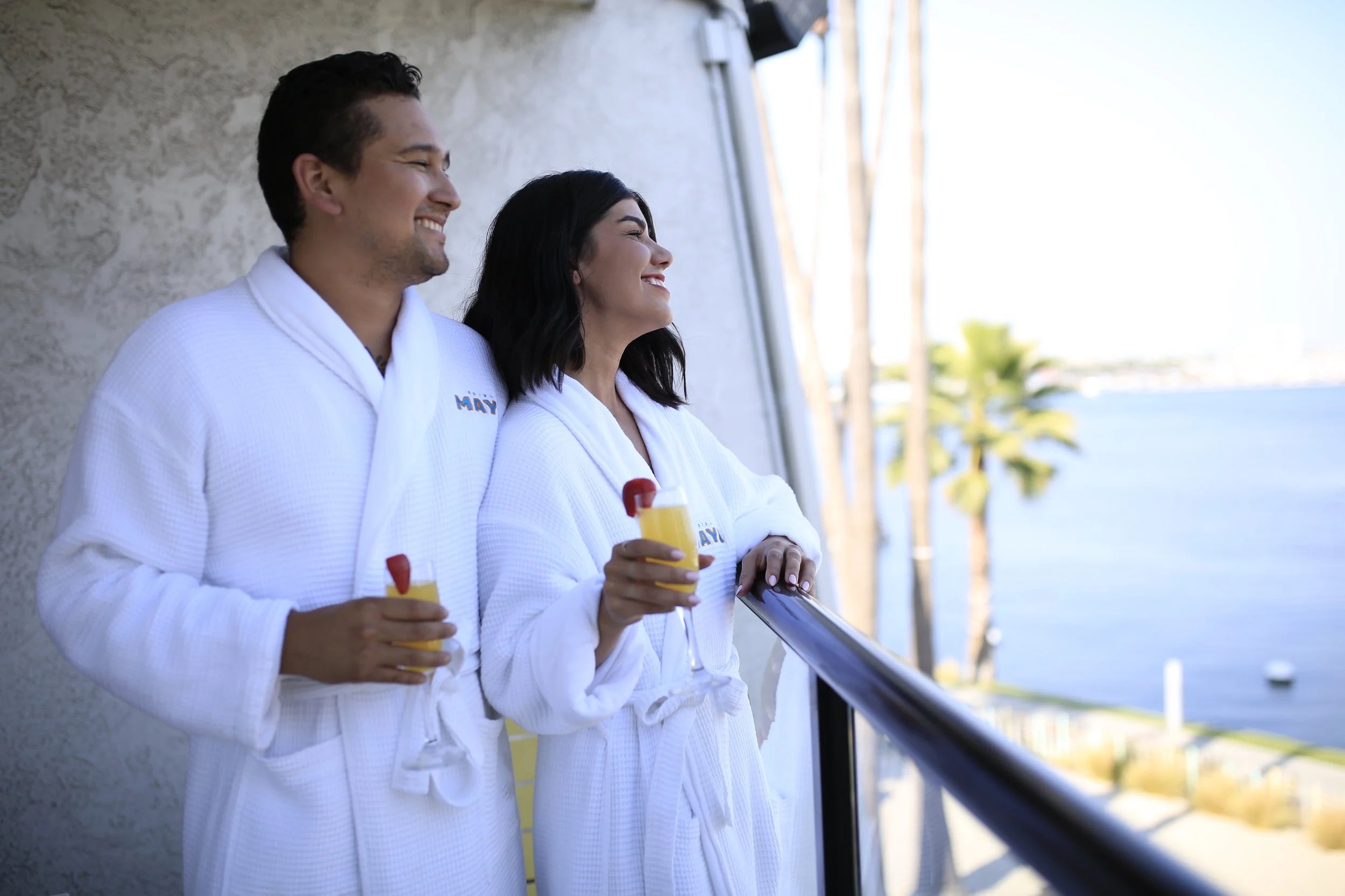 AN image of a male and female couple in white robes on a hotel balcony.